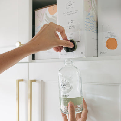 Person using a hand soap 3 litre refill box to refill a glass bottle
